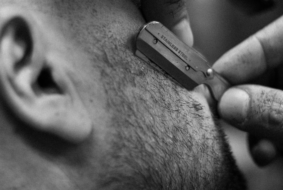 Gros plan en noir et blanc d’un rasoir droit en train de raser une barbe courte